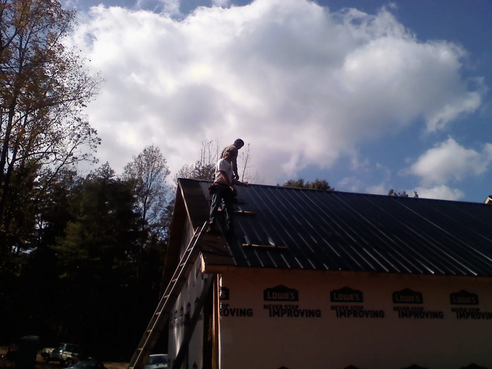 Roofer fastening dark metal panels high against a cloudy sky, from a Roof Inspection job in Lake City